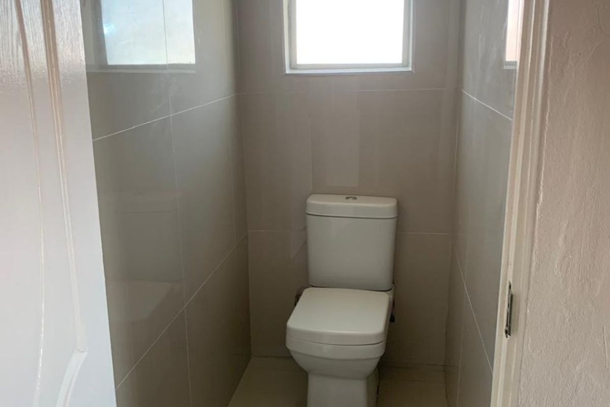 A compact, modern bathroom featuring neutral ceramic wall and floor tiles and a standard white toilet.