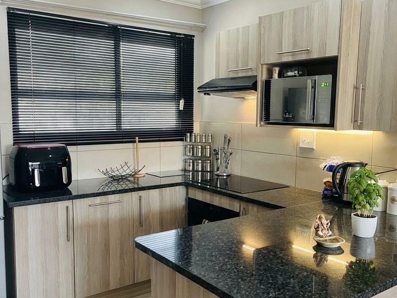 Modern kitchen featuring granite countertops, light wood-finish cabinetry, integrated appliances, and tiled flooring with ample natural light.