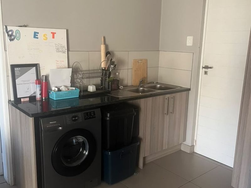 A functional laundry area featuring a double sink, granite countertop, and modern cabinetry with tiled flooring.