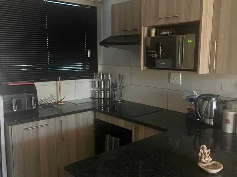 A functional kitchen featuring granite countertops, light wood-finish cabinetry, built-in microwave, extractor fan, and tiled backsplash with modern venetian blinds.