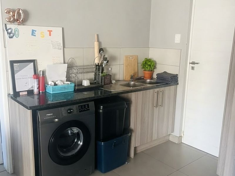 A functional laundry area featuring built-in cabinetry, granite countertops, a stainless steel double sink, and tiled flooring.
