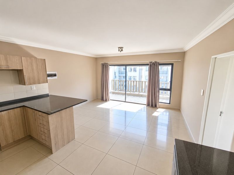 Spacious open-plan living area featuring modern kitchen cabinetry, granite countertops, tiled flooring, and large sliding doors leading to a private balcony.