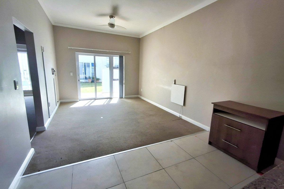 Spacious living area featuring a ceiling fan, sliding glass door access to the exterior, and a combination of tiled and carpeted flooring.