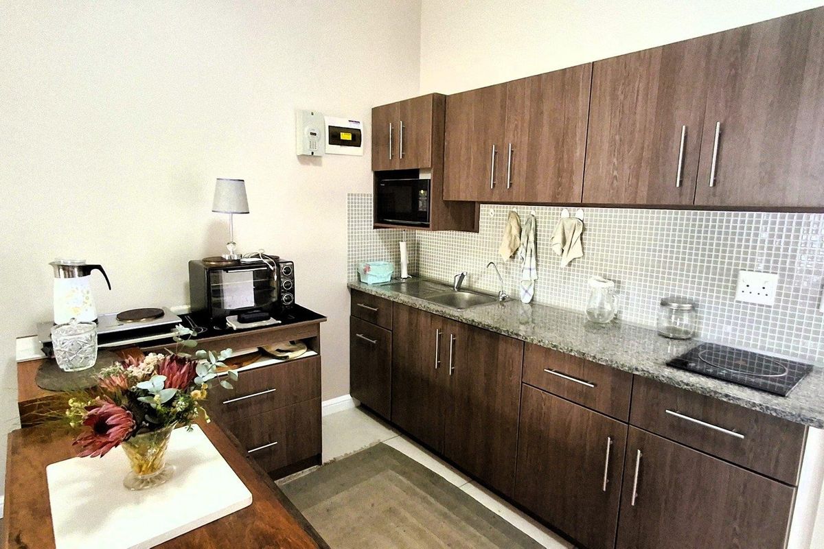 A functional kitchen featuring dark wood cabinetry, granite countertops, a mosaic tile backsplash, and integrated appliances including a microwave and electric cooktop.