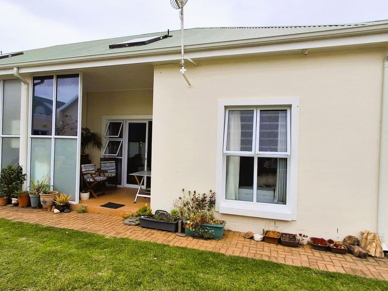 Rear view of the apartment featuring a covered patio area, brick paved walkway, and well-maintained exterior walls with aluminium window frames.