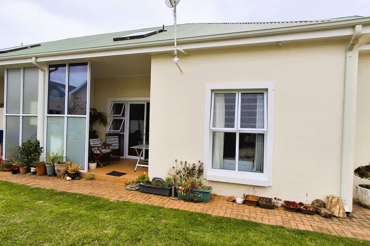 Rear view of the apartment featuring a covered patio area, brick paved walkway, and well-maintained exterior walls with aluminium window frames.