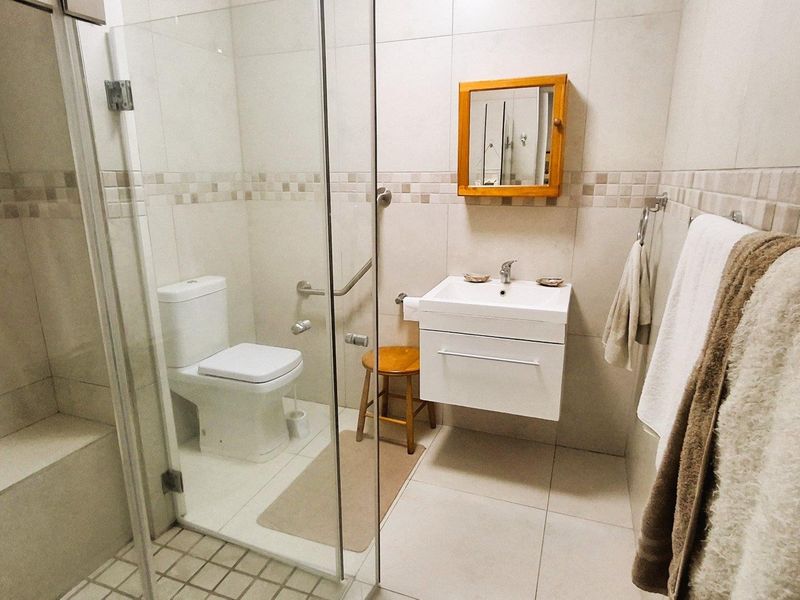 A clean and functional bathroom featuring a glass-enclosed shower, wall-mounted vanity with basin, and neutral tiled finishes throughout.