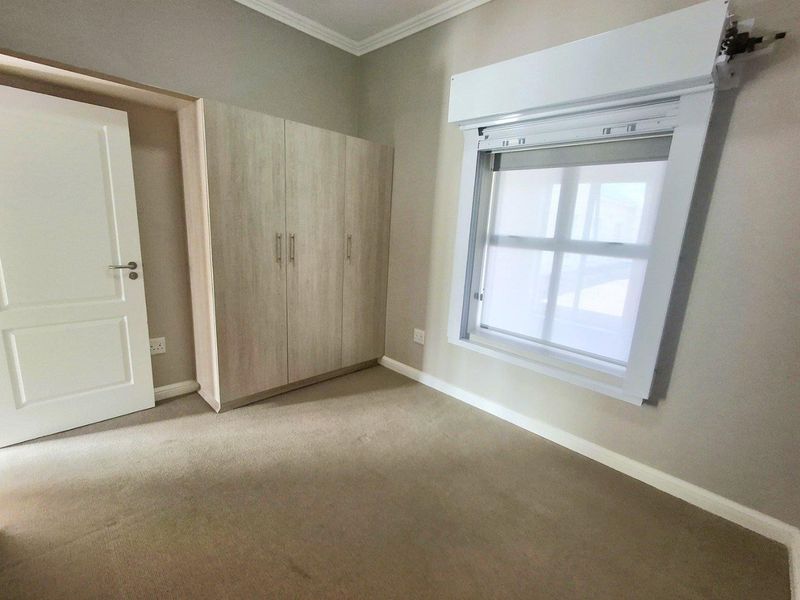 A clean, empty bedroom featuring neutral carpeting, built-in cupboards, and a window fitted with a security roller shutter.