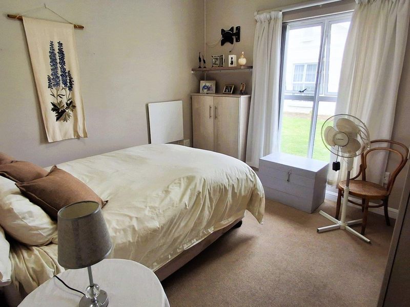 A functional bedroom featuring neutral carpeting, a built-in storage cupboard, a wall-mounted heater, and a window providing natural light.