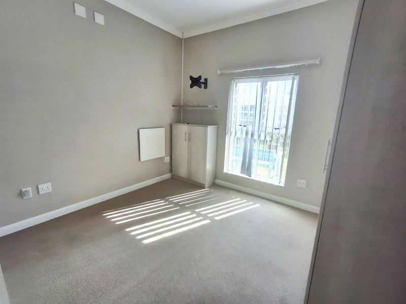 A neutral-toned bedroom featuring carpeted flooring, a built-in cupboard, and a wall-mounted TV bracket, offering a clean and functional space.