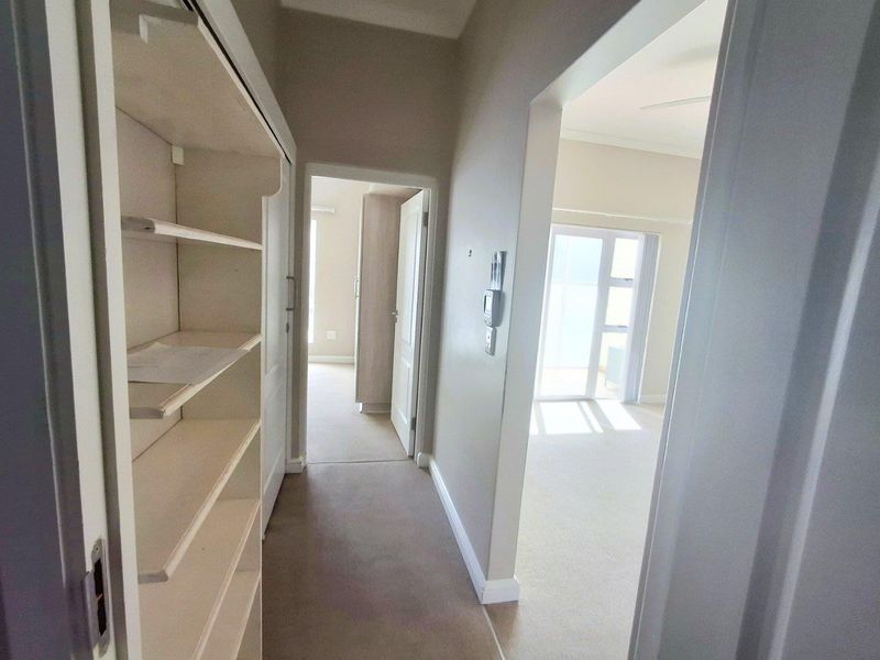 A bright, carpeted hallway featuring built-in shelving and access to adjacent rooms, providing a clean and functional transition space within the apartment.