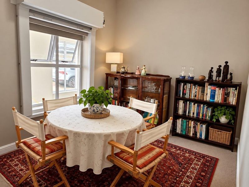 A well-maintained dining room featuring neutral walls, carpeted flooring, and a large window with a roller blind, providing a bright and functional space.