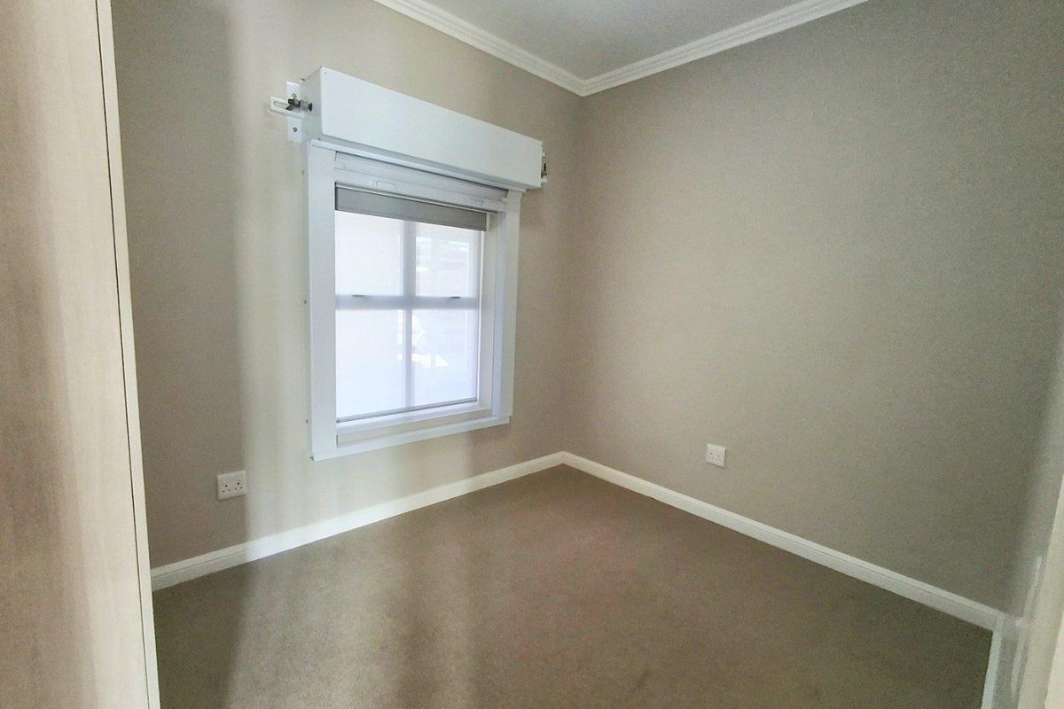 A clean, empty bedroom featuring neutral wall tones, carpeted flooring, and a window equipped with a functional roller shutter.