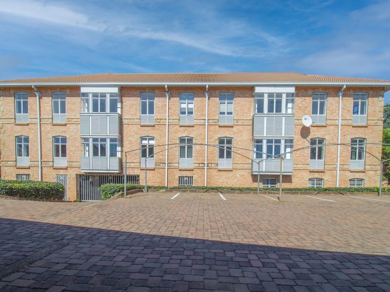 A well-maintained commercial building exterior featuring a classic brick facade, multiple bay windows, and a paved parking area with metal carport structures.