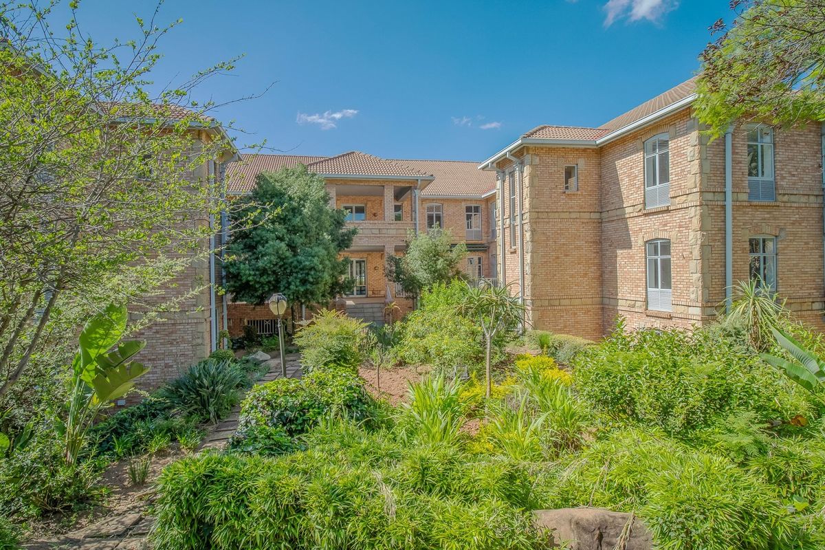 A view of the rear facade of a commercial building featuring face brick construction, tiled roofing, and a well-maintained landscaped garden with stone pathways.