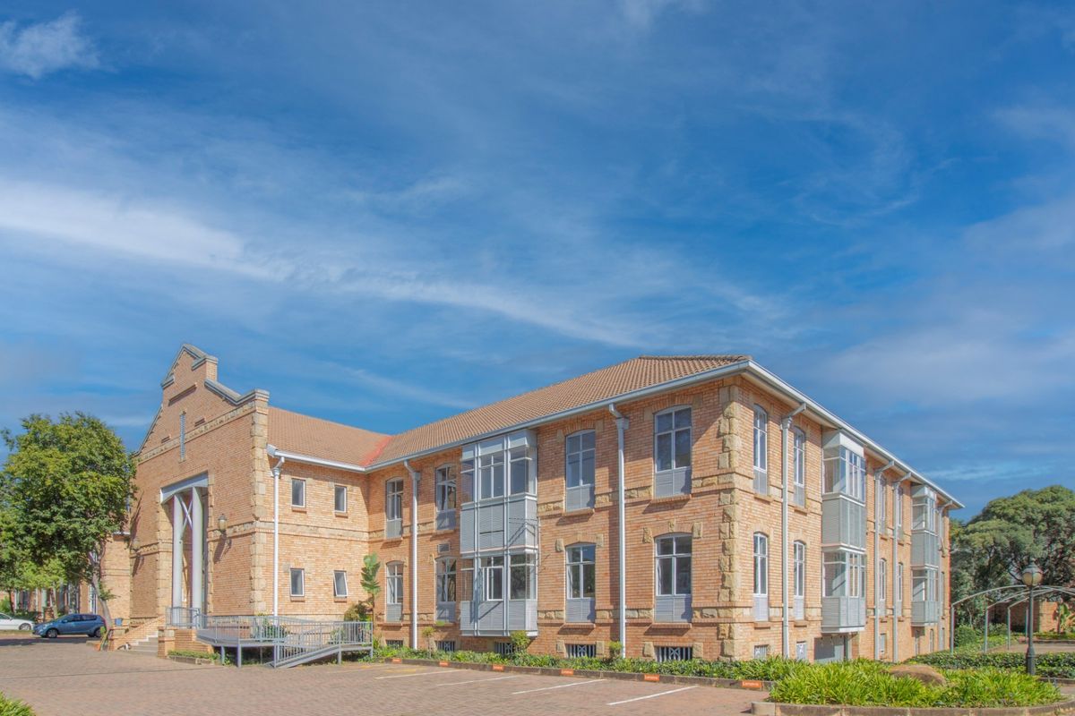 A well-maintained multi-story commercial building featuring a classic brick facade, tiled roof, and bay windows with an adjacent paved parking area.