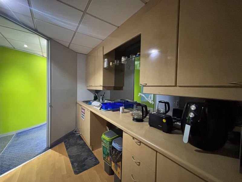 A functional office kitchenette featuring built-in laminate cabinetry, a stainless steel sink, and a mirrored backsplash, providing essential utility space for staff.