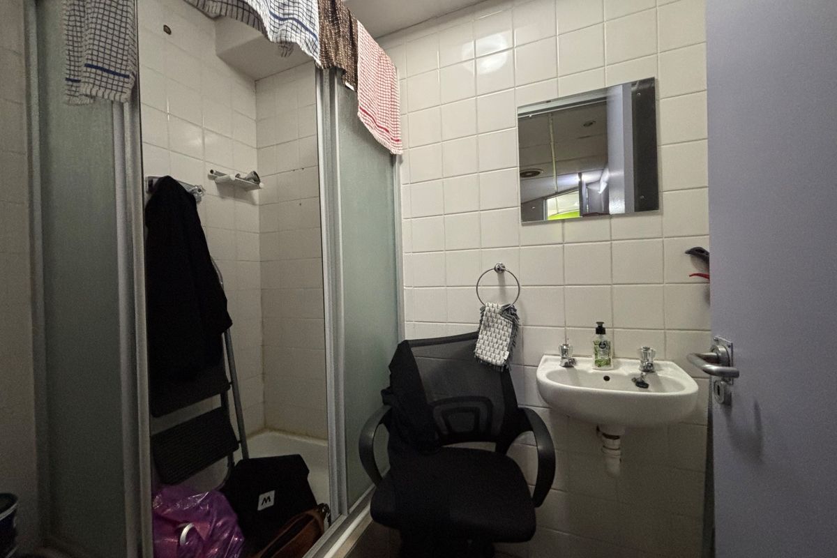 A compact bathroom featuring a shower enclosure, wall-mounted basin, and tiled walls, requiring some maintenance and cosmetic updates.
