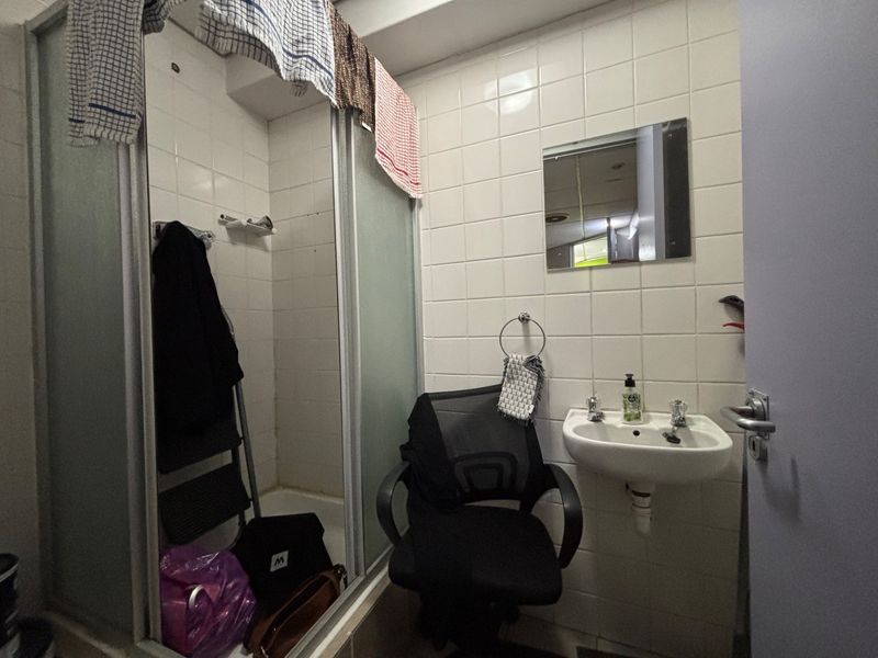 A compact bathroom featuring a shower enclosure, wall-mounted basin, and tiled walls, requiring some maintenance and cosmetic updates.