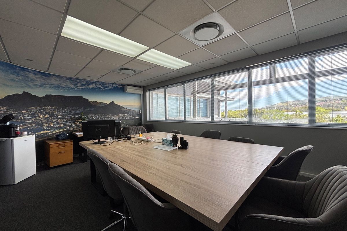 A professional office meeting room featuring a suspended ceiling, large windows with venetian blinds, and integrated air conditioning.