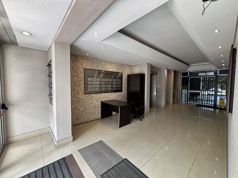 A professional office building lobby featuring tiled floors, a stone accent wall with directory signage, recessed lighting, and a secure elevator access point.