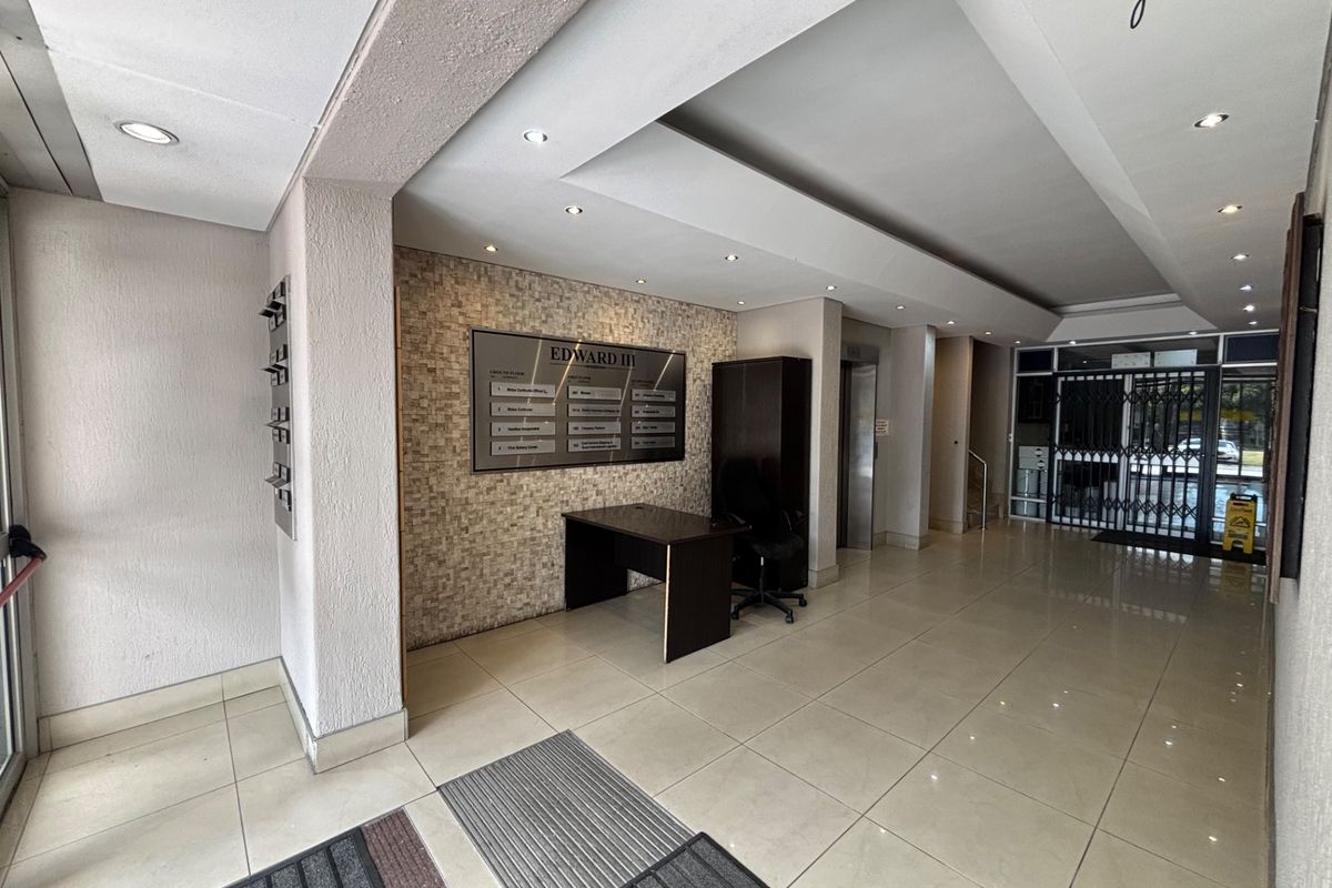 A professional office building lobby featuring tiled floors, a stone accent wall with directory signage, recessed lighting, and a secure elevator access point.