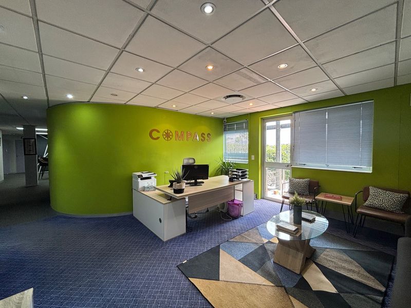 A professional office space featuring a curved feature wall, suspended ceiling with recessed lighting, and direct access to an outdoor area via a glass door.