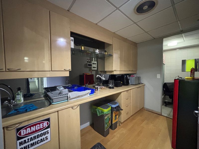 A functional office kitchenette featuring laminate cabinetry, a stainless steel sink, and drop ceiling tiles, providing essential utility space for staff.