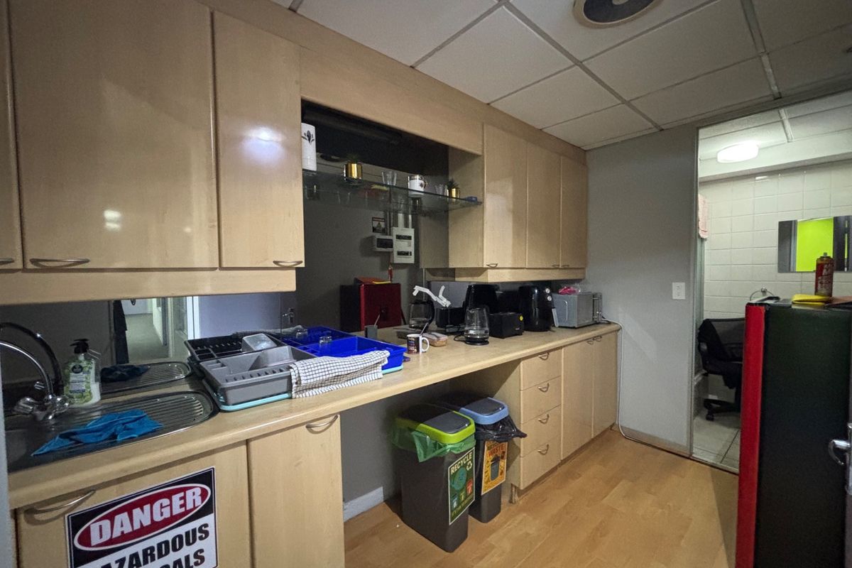 A functional office kitchenette featuring laminate cabinetry, a stainless steel sink, and drop ceiling tiles, providing essential utility space for staff.