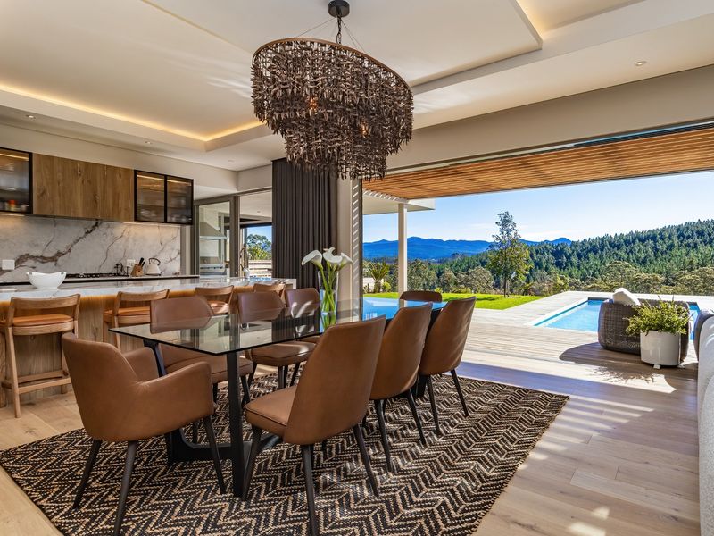 Luxurious open-plan living and dining area featuring a modern kitchen, seamless indoor-outdoor flow to a deck with pool, and stunning mountain views.