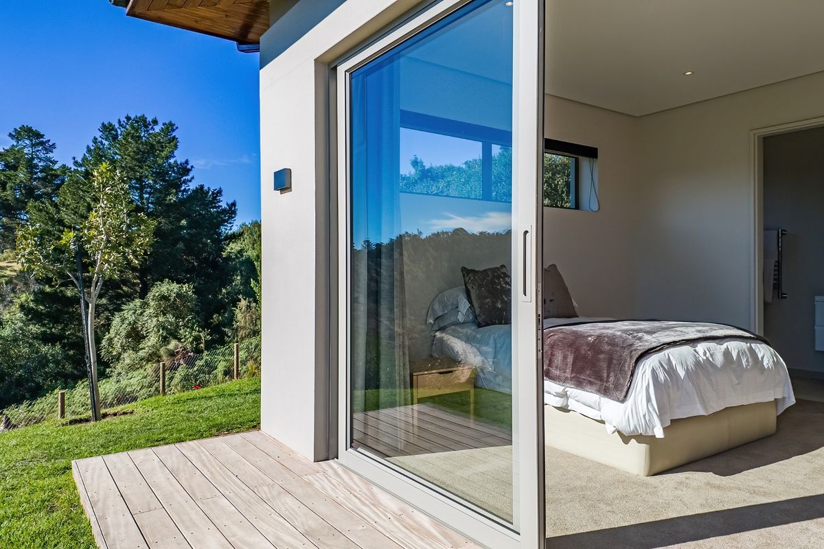 Modern bedroom featuring large sliding glass doors that open onto a private timber deck with scenic garden views.