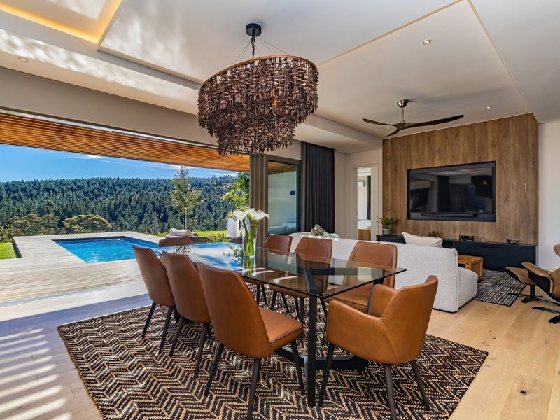 Spacious open-plan living and dining area featuring hardwood floors, a timber feature wall, and seamless indoor-outdoor flow to the pool deck and forest views.