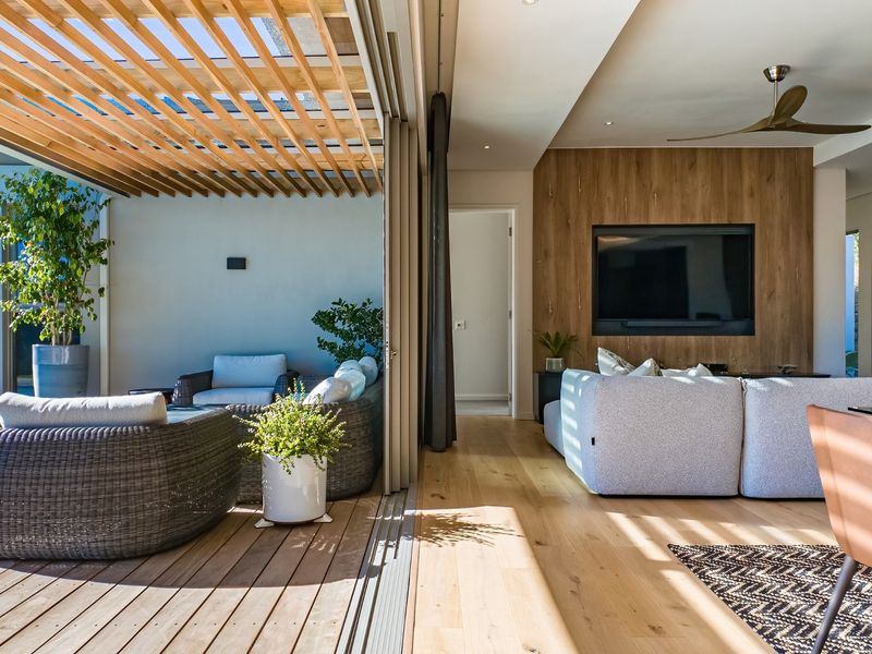 Modern open-plan living area featuring seamless indoor-outdoor flow to a covered timber deck with pergola, complemented by high-end finishes and hardwood flooring.