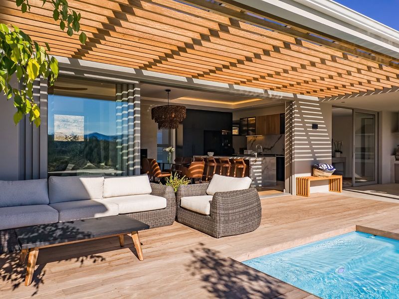 A modern covered patio featuring timber decking and a pergola, seamlessly connecting to the swimming pool and open-plan interior living space.
