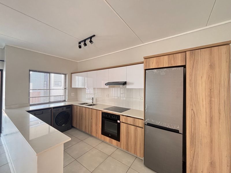 Modern kitchen featuring wood-finish cabinetry, stone countertops, integrated electric hob and oven, and tiled flooring in a clean, well-maintained space.