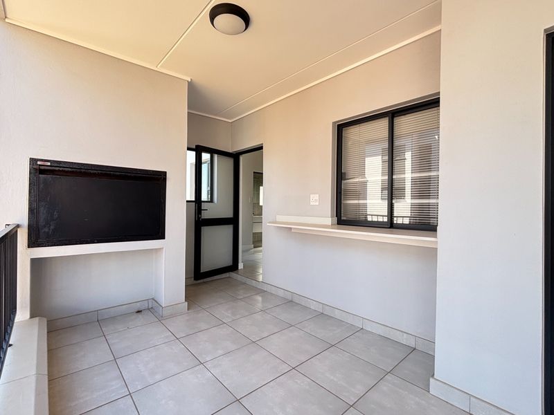 A clean, covered balcony featuring a built-in braai, tiled flooring, and a convenient serving ledge, perfect for outdoor entertaining.