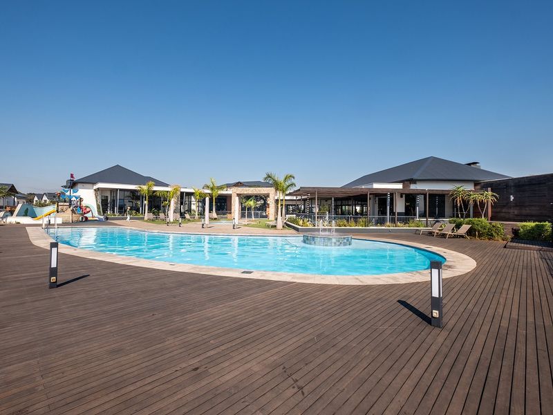 A well-maintained communal pool area featuring extensive timber decking, a central water feature, and surrounding covered patio spaces.