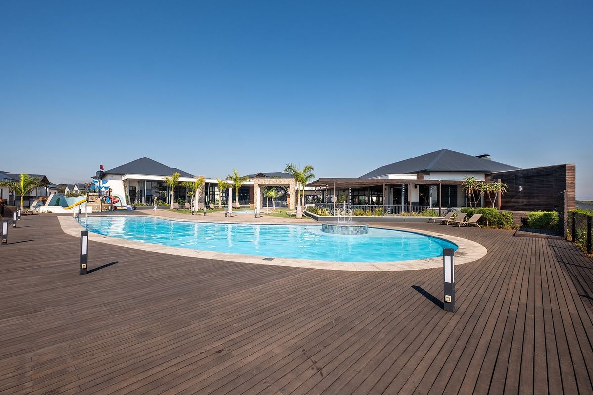 A well-maintained communal pool area featuring extensive timber decking, a central water feature, and surrounding covered patio spaces.