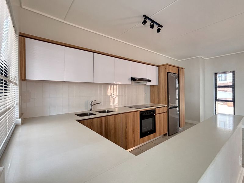 Modern kitchen featuring sleek wood-grain and white cabinetry, stone countertops, integrated appliances, and a clean tiled backsplash in a bright, open-plan layout.