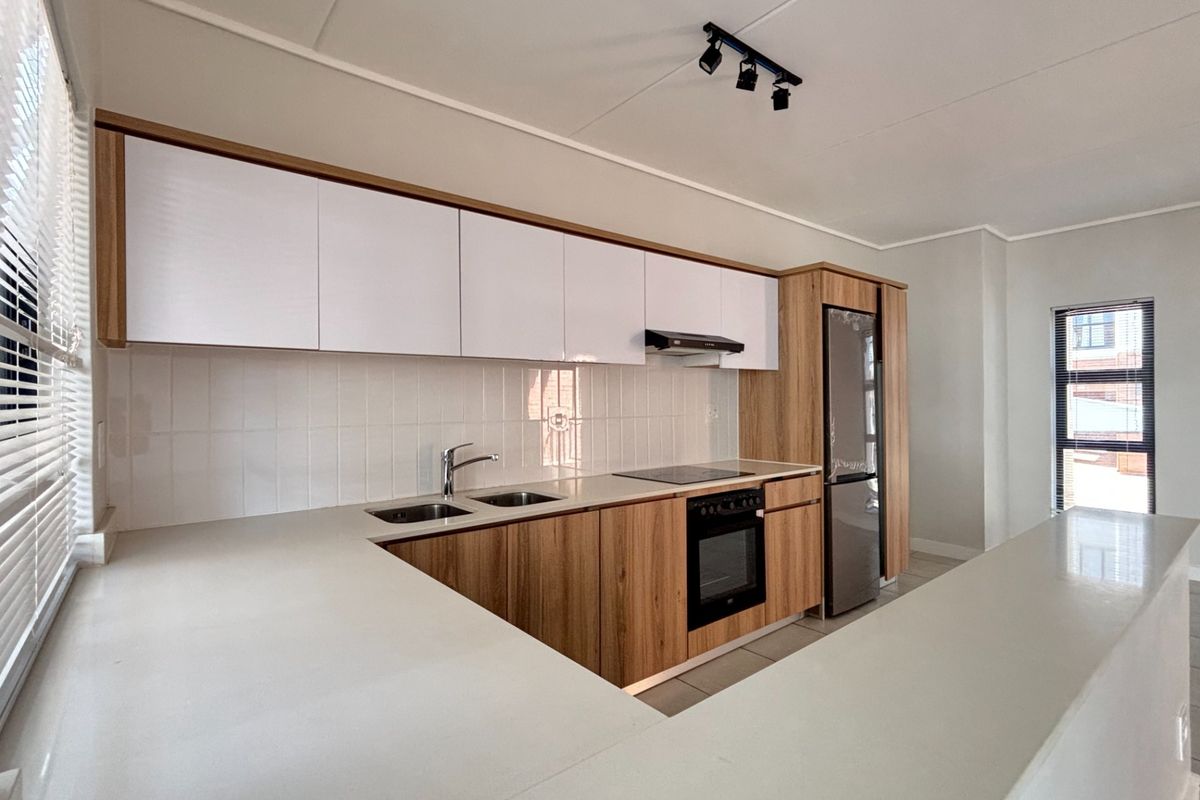 Modern kitchen featuring sleek wood-grain and white cabinetry, stone countertops, integrated appliances, and a clean tiled backsplash in a bright, open-plan layout.
