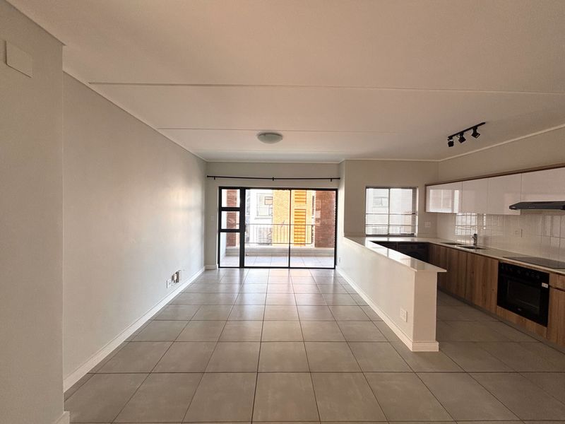 Spacious open-plan living and kitchen area featuring modern cabinetry, integrated appliances, tiled flooring, and a sliding door leading to a balcony.