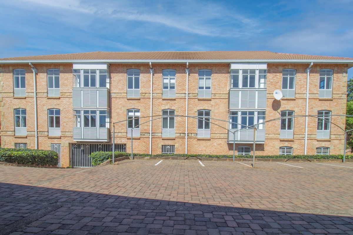 A well-maintained commercial building exterior featuring a classic brick facade, multiple bay windows, and a paved parking area with metal carport structures.
