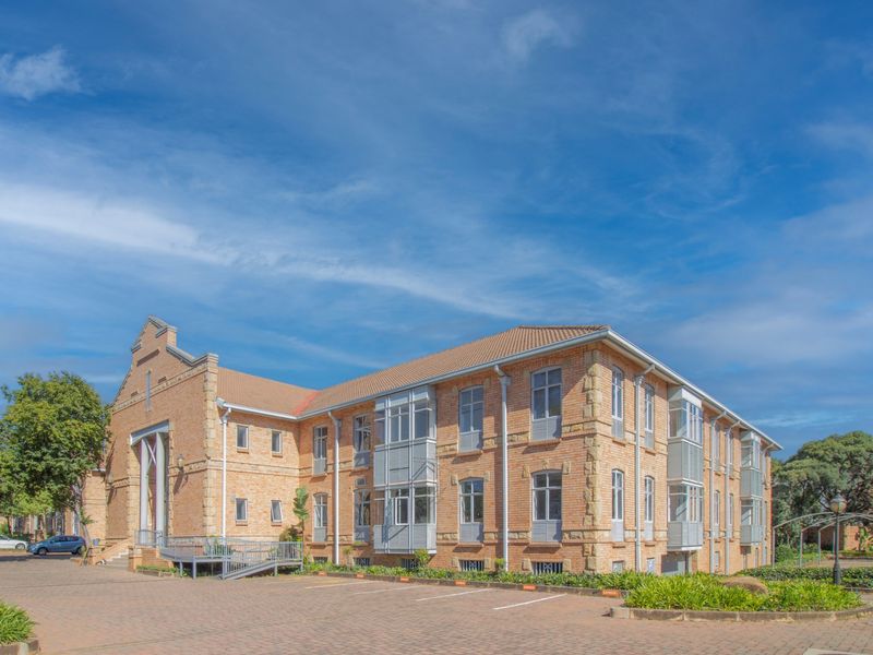A well-maintained multi-story commercial building featuring a classic brick facade, tiled roof, and bay windows with an adjacent paved parking area.