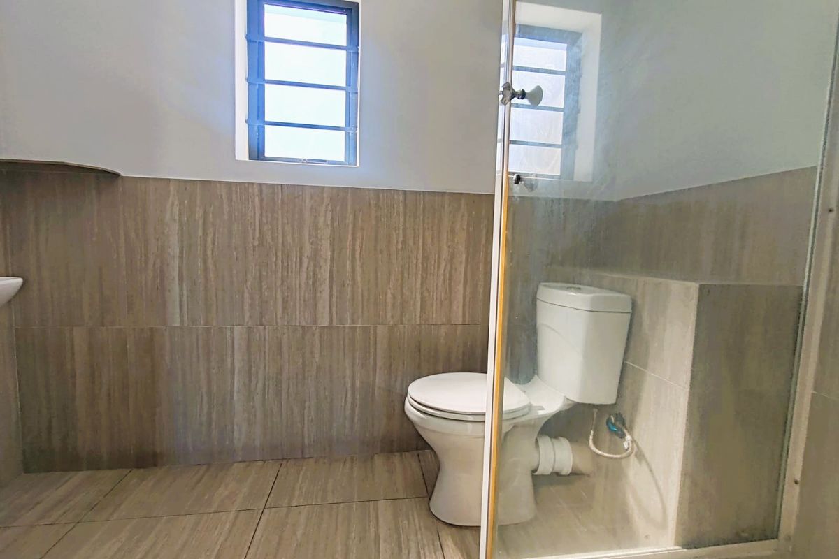 A functional bathroom featuring tiled walls and flooring, a standard toilet, and a glass-enclosed shower area.