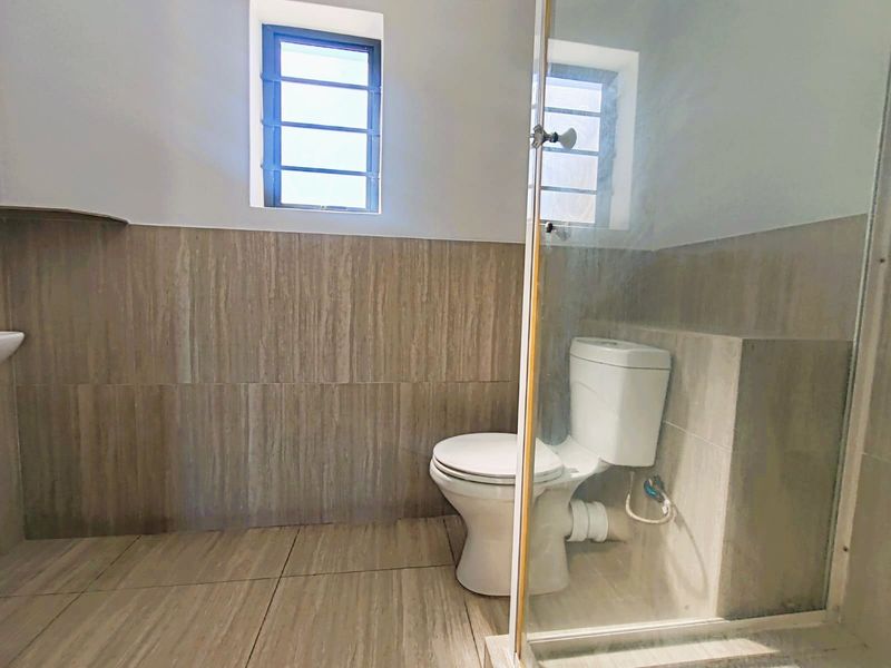 A functional bathroom featuring tiled walls and flooring, a standard toilet, and a glass-enclosed shower area.