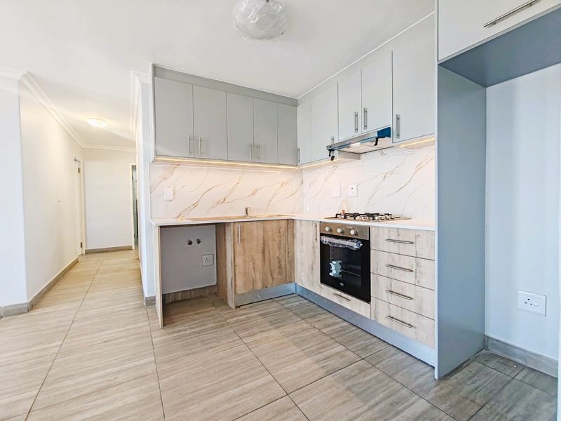 Modern kitchen featuring light wood and grey cabinetry, marble-look splashback, built-in gas hob, oven, and extractor fan with tiled flooring.