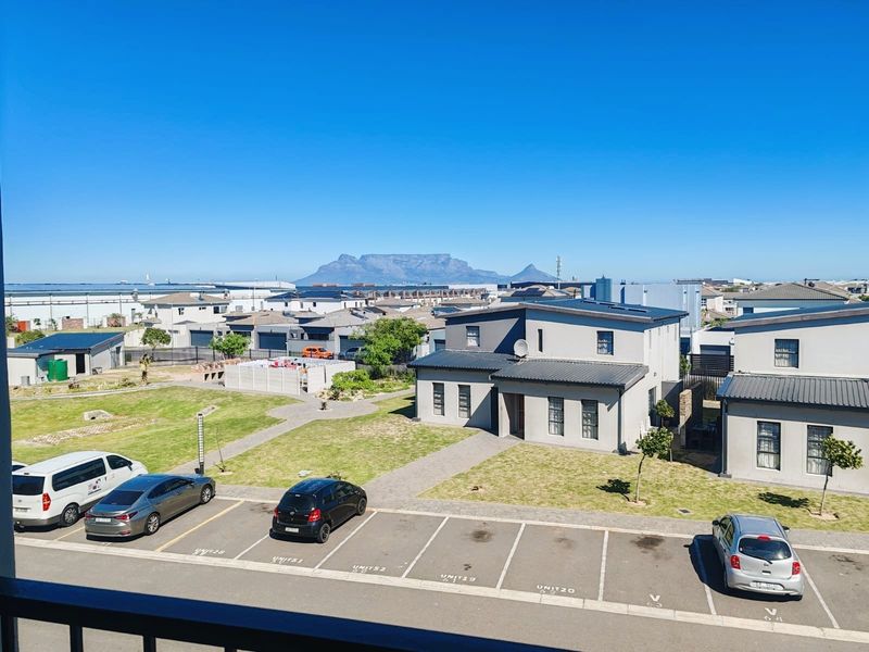 Elevated view overlooking a residential complex with paved parking, communal garden areas, and a clear view of Table Mountain in the distance.