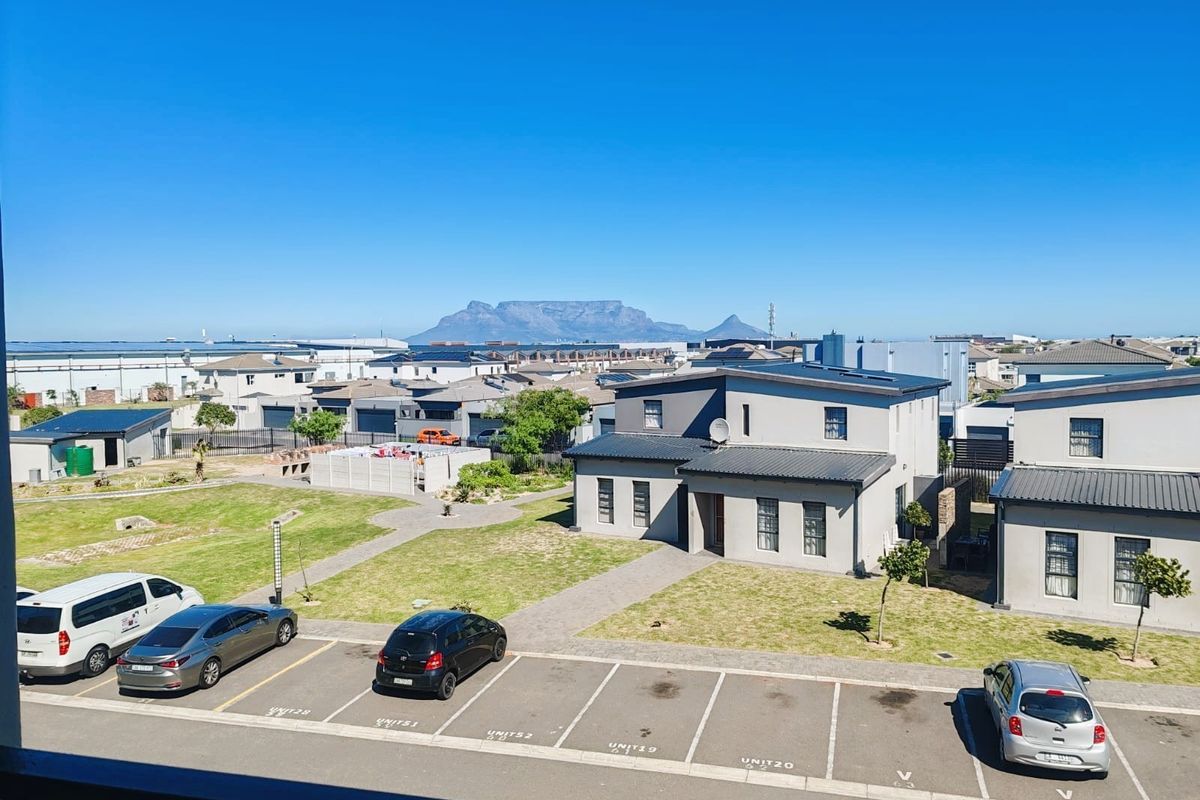 Elevated view overlooking a residential complex with paved parking, communal garden areas, and a clear view of Table Mountain in the distance.