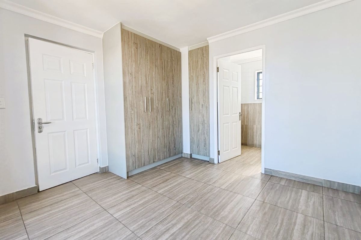 A clean, empty bedroom featuring modern wood-look tiled flooring and built-in cupboards, offering a neutral and well-maintained space ready for personalization.