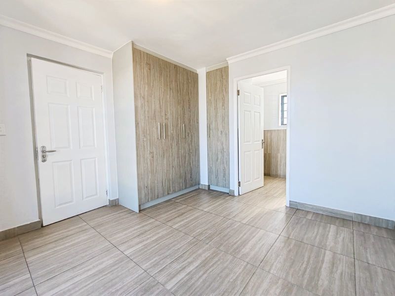 A clean, empty bedroom featuring modern wood-look tiled flooring and built-in cupboards, offering a neutral and well-maintained space ready for personalization.